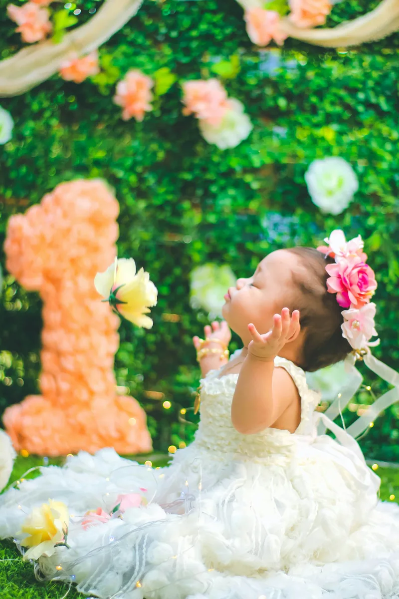 First birthday portrait in a white tulle dress before a floral backdrop