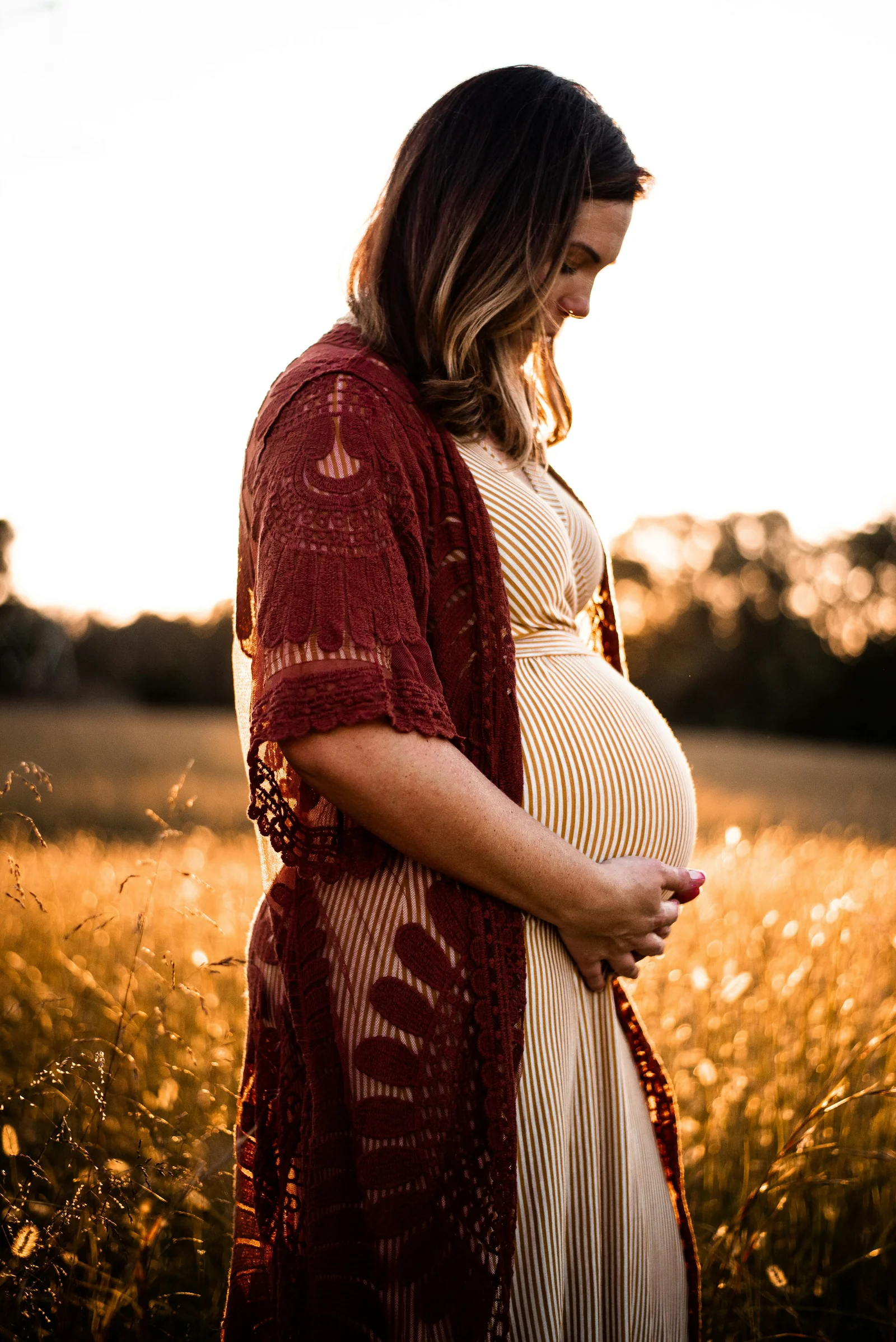Expecting mother in a wine-red cardigan at golden hour in a meadow
