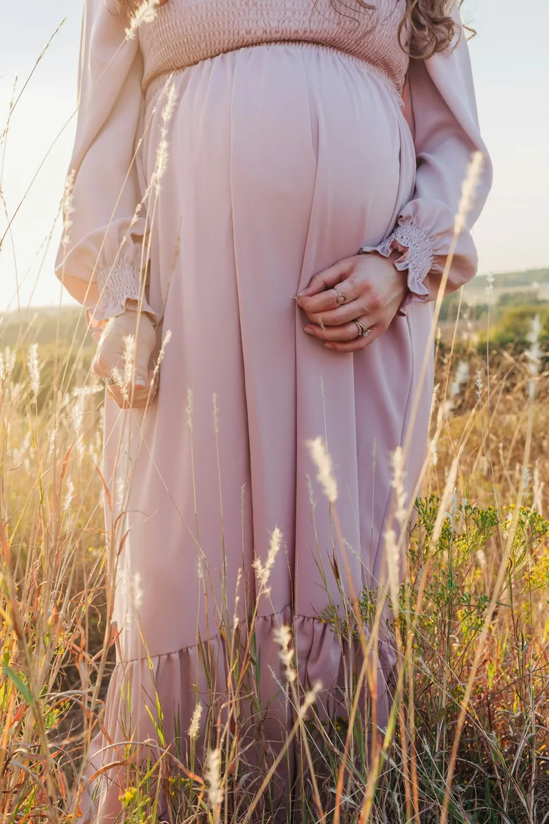 Close portrait of a pregnant belly in a blush dress among tall grasses