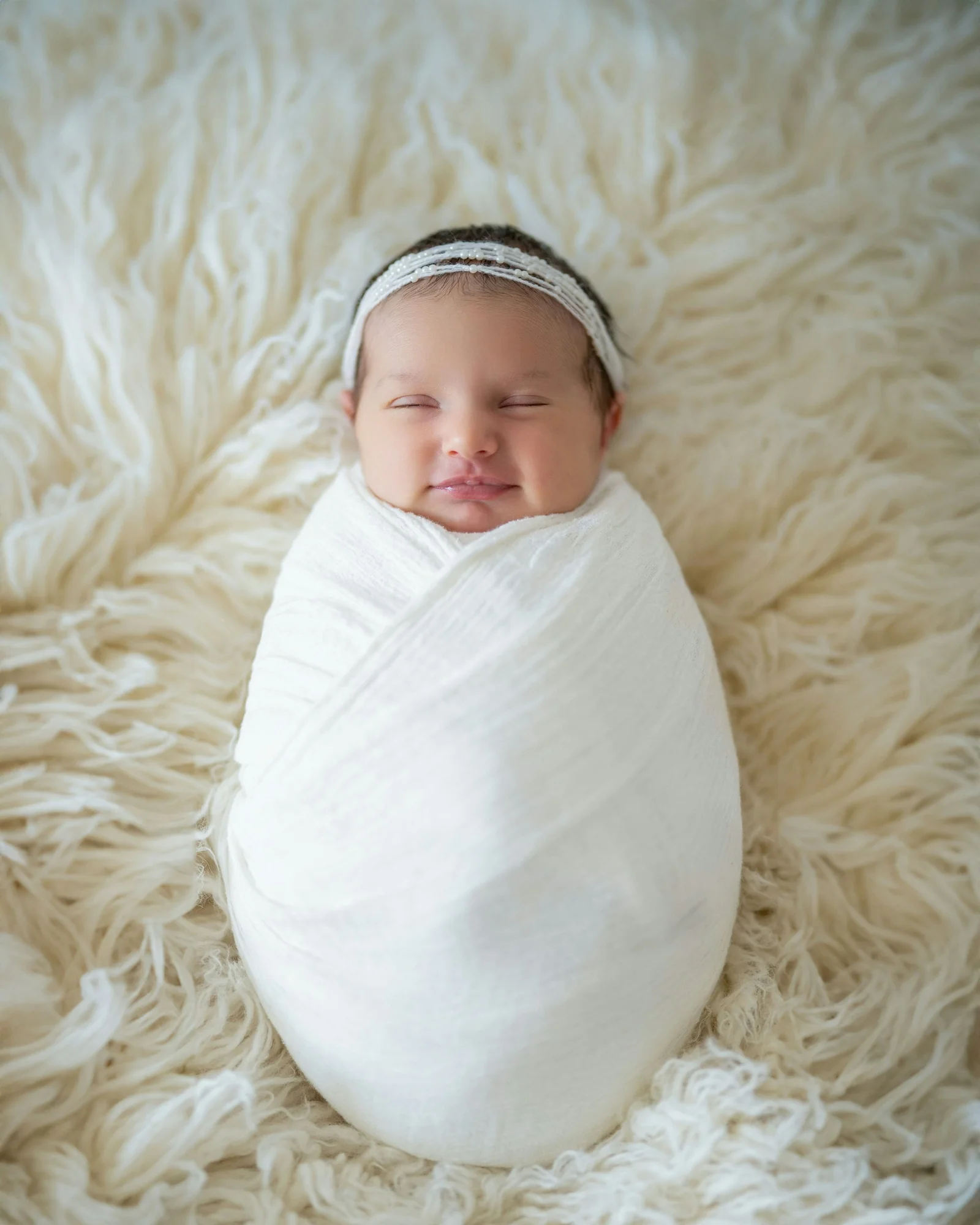 Newborn asleep in a cream swaddle on a soft sheepskin
