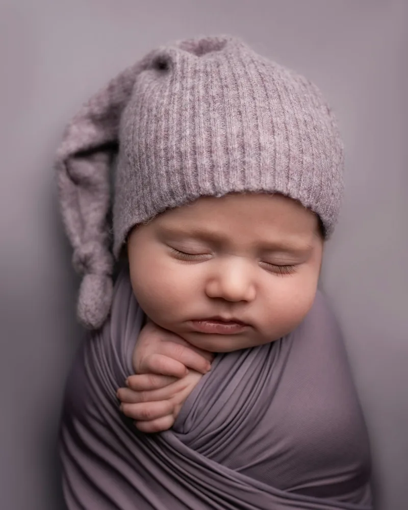 Sleeping newborn in a mauve knit cap and wrap