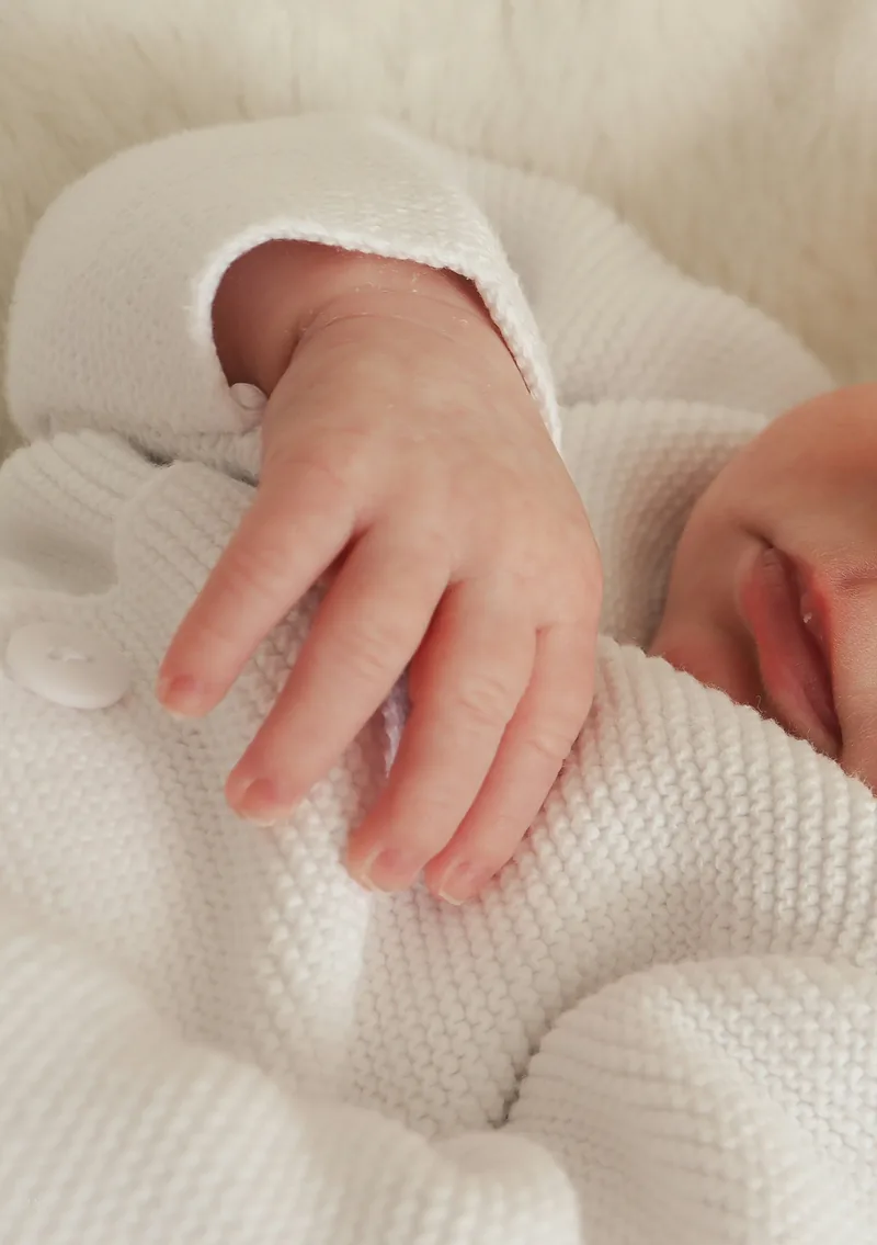 Close detail of a newborn's hand on a cream knit blanket