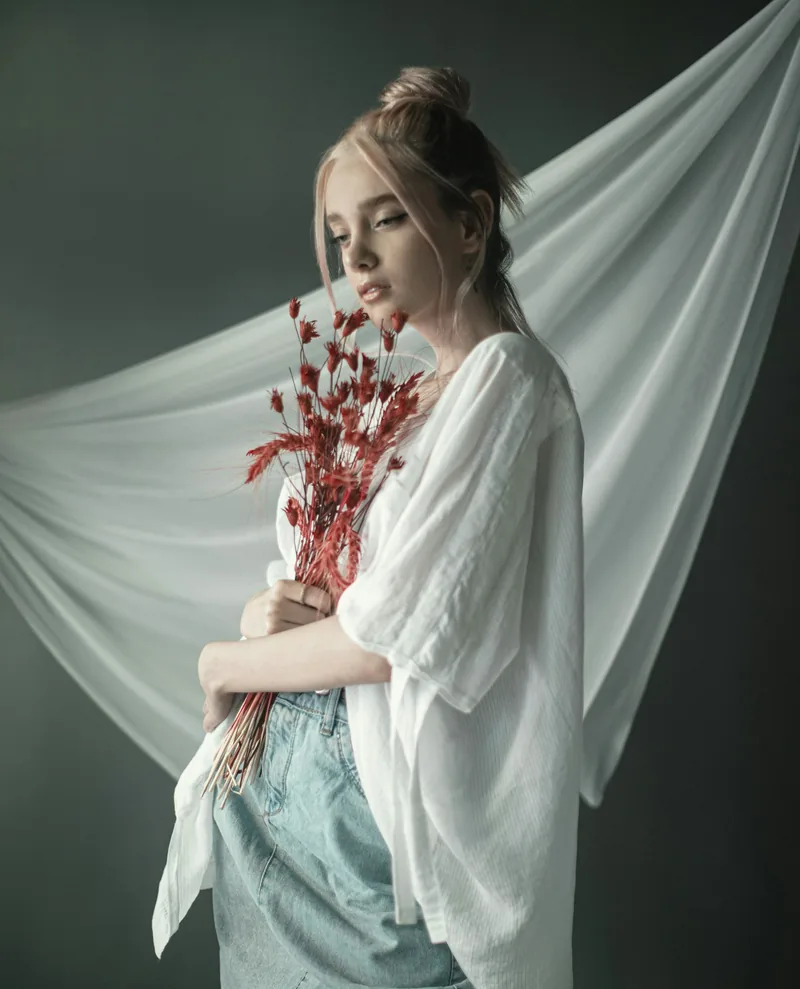 Woman holding red dried florals before a flowing white drape