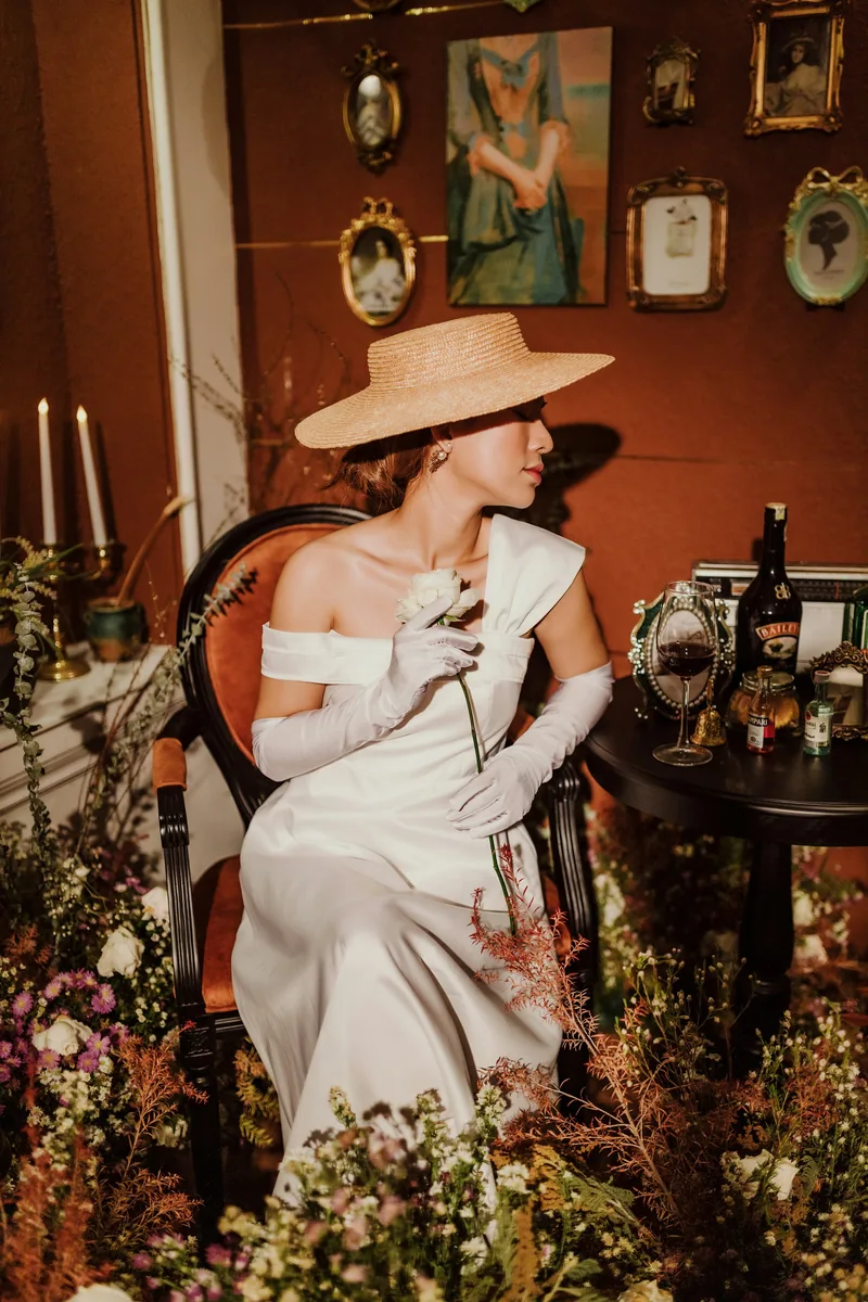 Woman in a white gown and hat on a styled vintage set