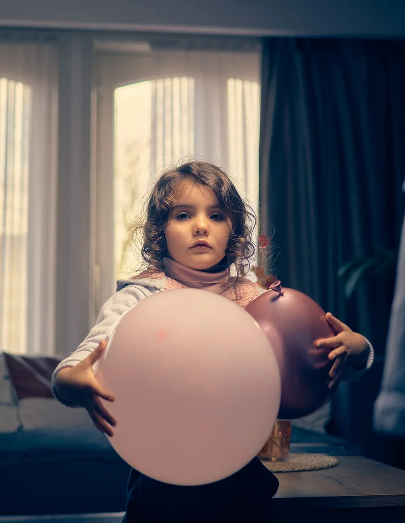 Child holding a large pink balloon in soft window light