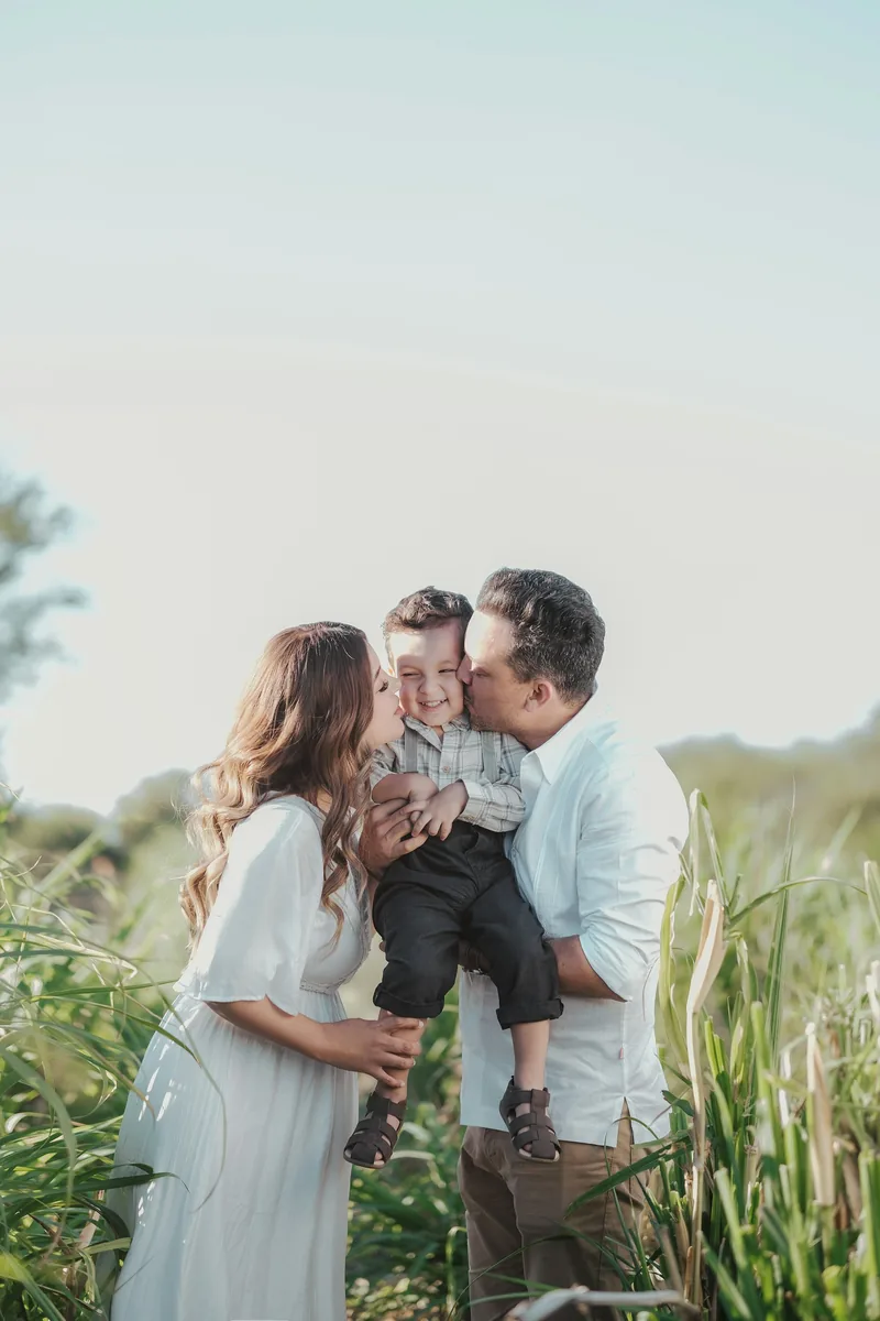 Parents kissing their little boy in a sunlit meadow